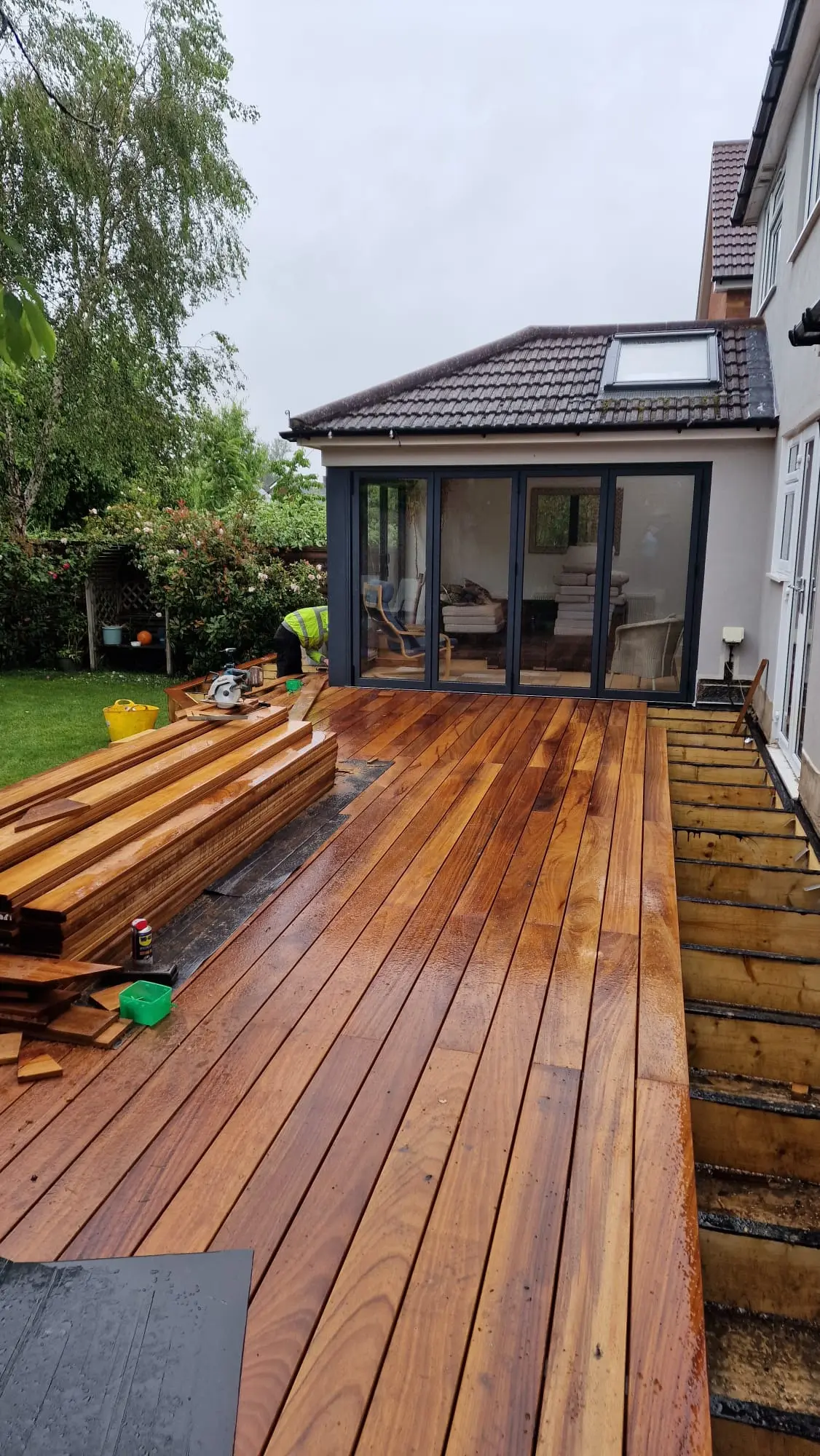 Freshly laid hardwood decking, wet with rain, running up to bifold doors