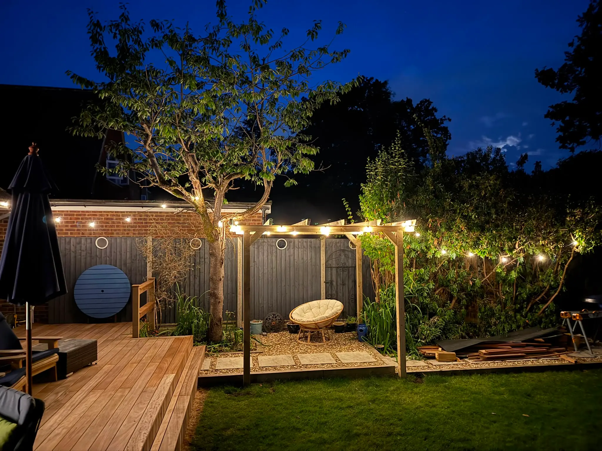 A hardwood deck and timber pergola lit by festoon lights at dusk