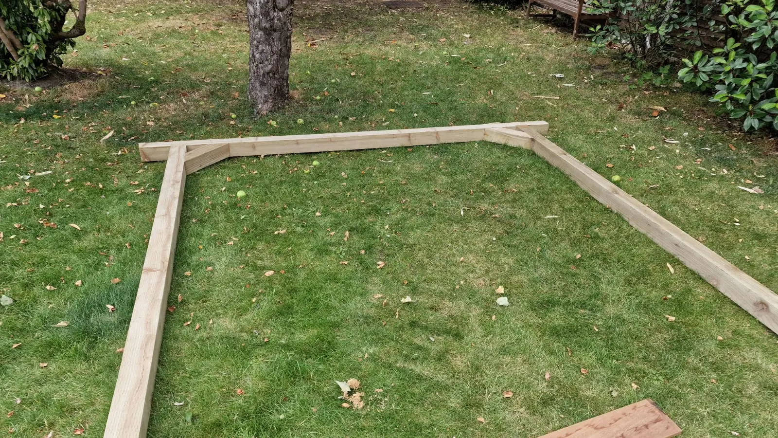 Timber frame being set out on a large lawn under mature trees